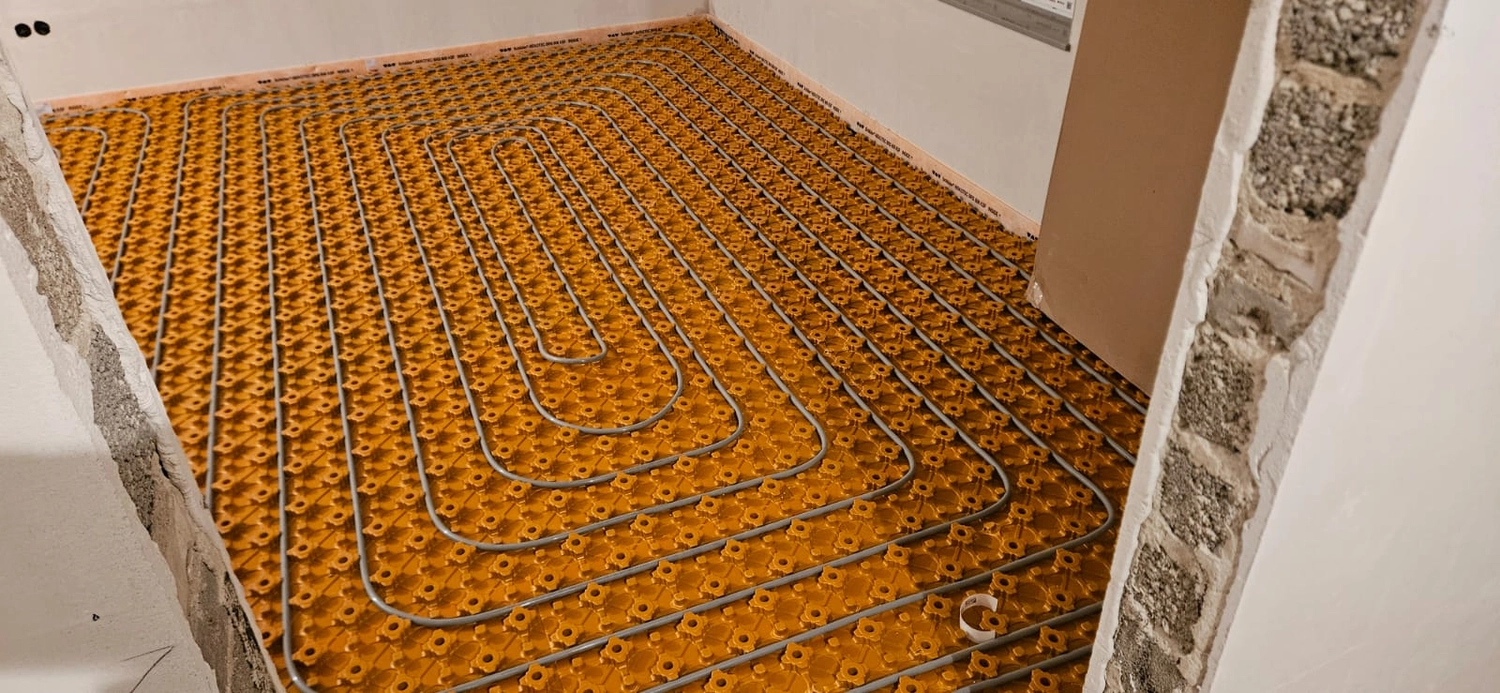 Fißmann - Heizung Sanitär Lüftung - Hydronisches Strahlungsheizungssystem, das die Installation von Rohren auf speziellen Noppenplatten vor dem Gießen des Betonestrichs zeigt.