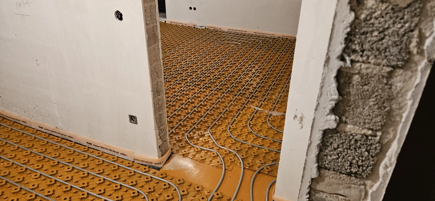 Fißmann - Heizung Sanitär Lüftung - Hydronisches Strahlungsheizungssystem, das die Installation von Rohren auf speziellen Noppenplatten vor dem Gießen des Betonestrichs zeigt.