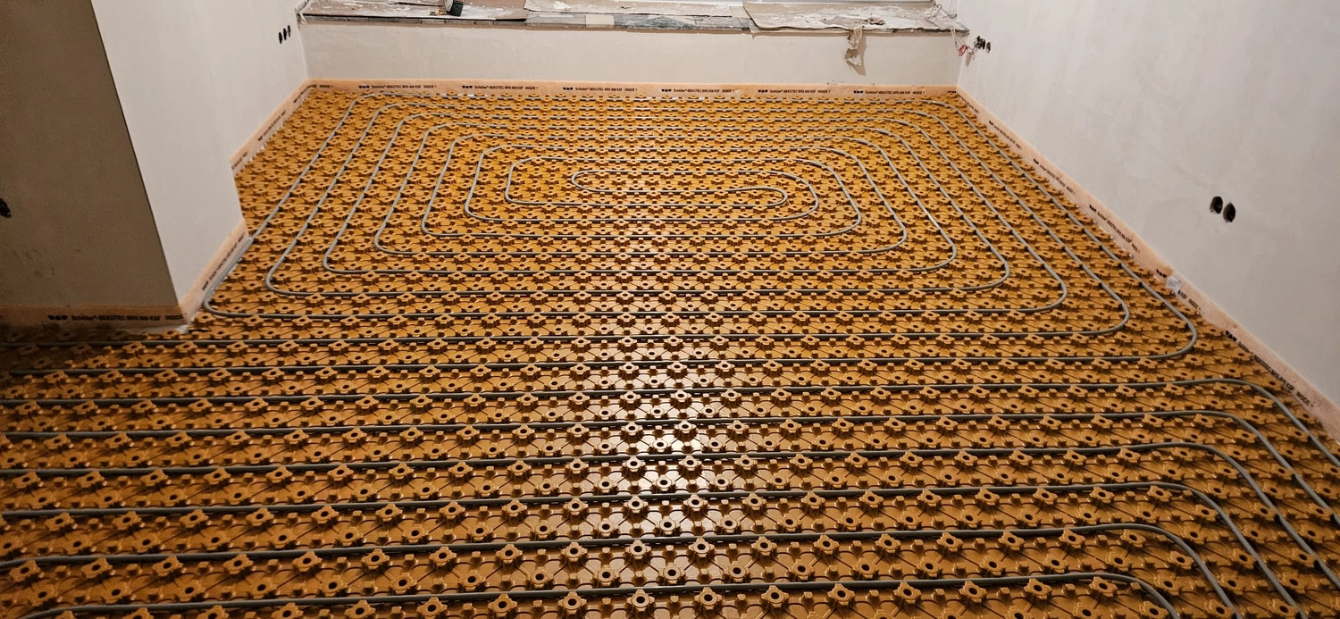 Fißmann - Heizung Sanitär Lüftung - Hydronisches Strahlungsheizungssystem, das die Installation von Rohren auf speziellen Noppenplatten vor dem Gießen des Betonestrichs zeigt.