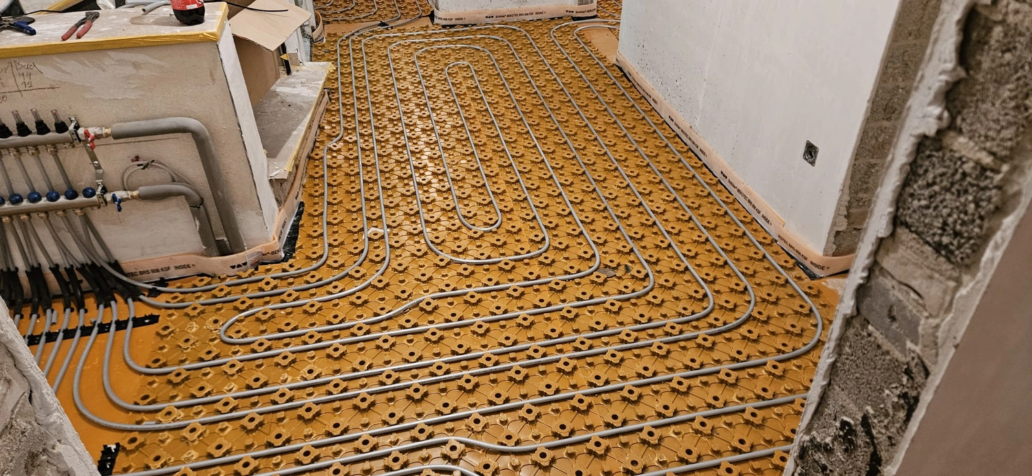 Fißmann - Heizung Sanitär Lüftung - Hydronisches Strahlungsheizungssystem, das die Installation von Rohren auf speziellen Noppenplatten vor dem Gießen des Betonestrichs zeigt.