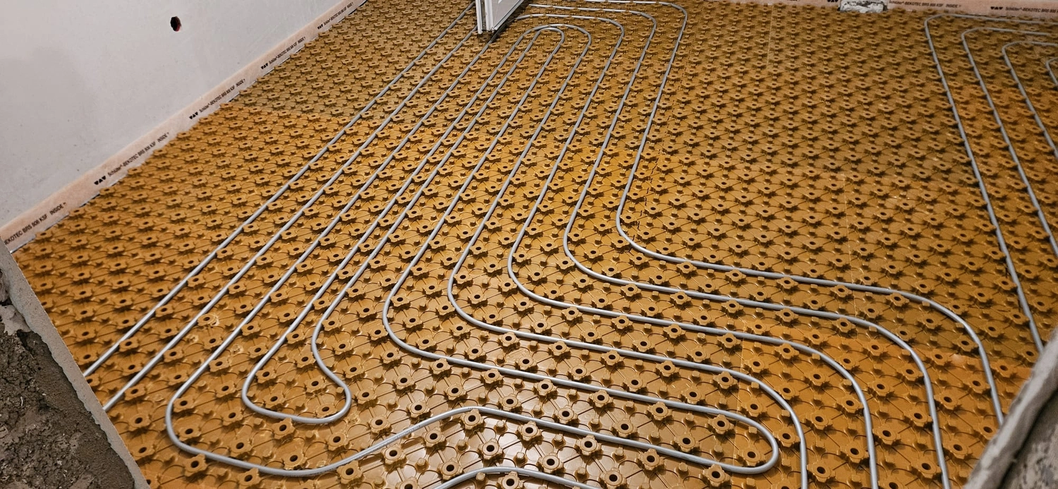 Fißmann - Heizung Sanitär Lüftung - Hydronisches Strahlungsheizungssystem, das die Installation von Rohren auf speziellen Noppenplatten vor dem Gießen des Betonestrichs zeigt.
