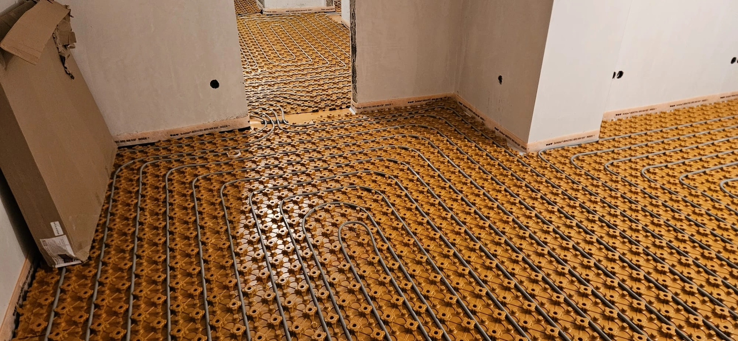 Fißmann - Heizung Sanitär Lüftung - Hydronisches Strahlungsheizungssystem, das die Installation von Rohren auf speziellen Noppenplatten vor dem Gießen des Betonestrichs zeigt.