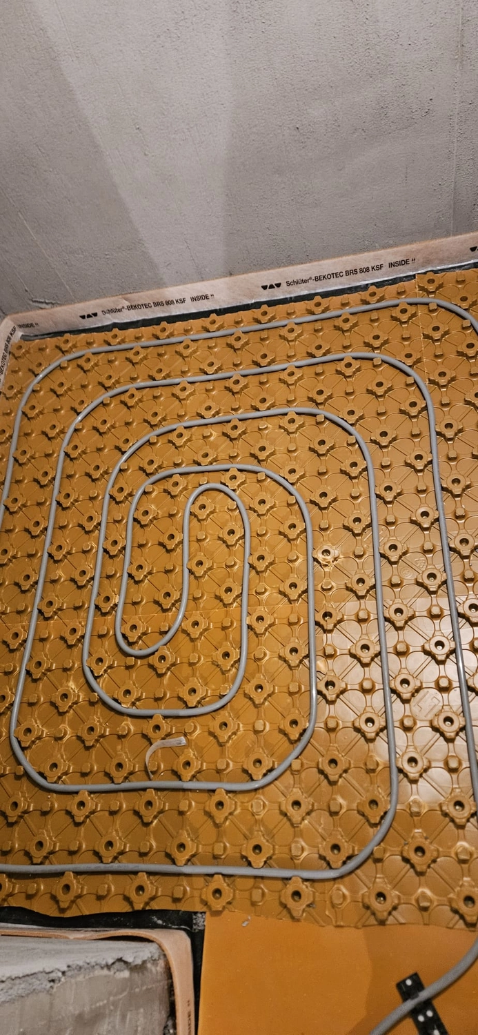Fißmann - Heizung Sanitär Lüftung - Hydronisches Strahlungsheizungssystem, das die Installation von Rohren auf speziellen Noppenplatten vor dem Gießen des Betonestrichs zeigt.