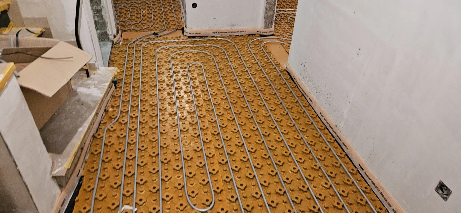Fißmann - Heizung Sanitär Lüftung - Hydronisches Strahlungsheizungssystem, das die Installation von Rohren auf speziellen Noppenplatten vor dem Gießen des Betonestrichs zeigt.