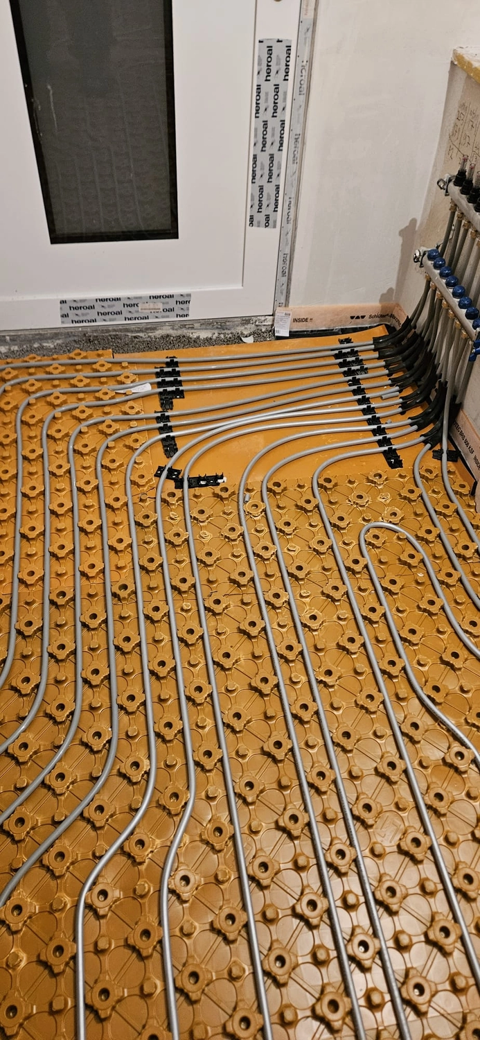 Fißmann - Heizung Sanitär Lüftung - Hydronisches Strahlungsheizungssystem, das die Installation von Rohren auf speziellen Noppenplatten vor dem Gießen des Betonestrichs zeigt.